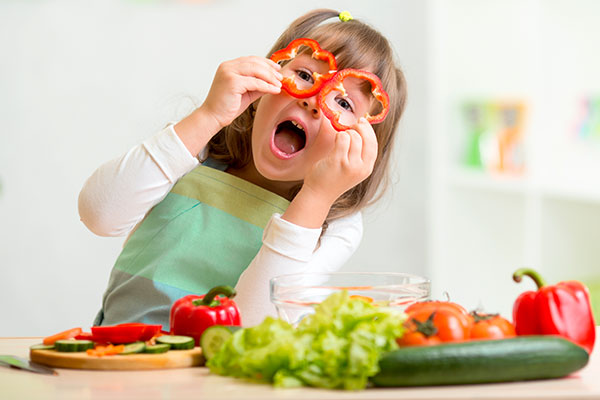 Kind mit frischem Sommergemüse, hält sich zwei rote Paprikaringe vor die Augen